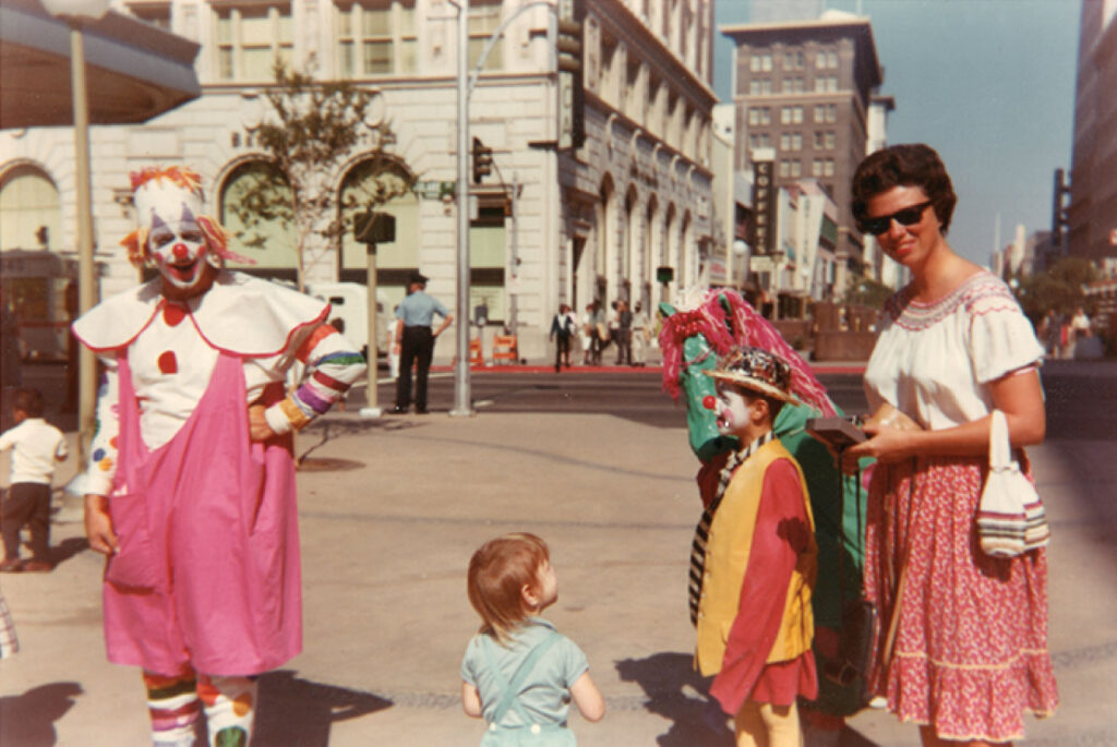 Dan Pessano (left) dressed as "Mr. Pink" and Dr. Janet Loring (right) in downtown Fresno circa 1965. A child is also dressed as a clown and a toddler loooks up at him between Mr. Pinnk and Loring.