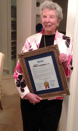 Dr. Janet Loring holding a City of Fresno proclamation honoring her 90th birthday. She is wearing black slacks and shirt with a jacket with pink, white and nearly black flowers.