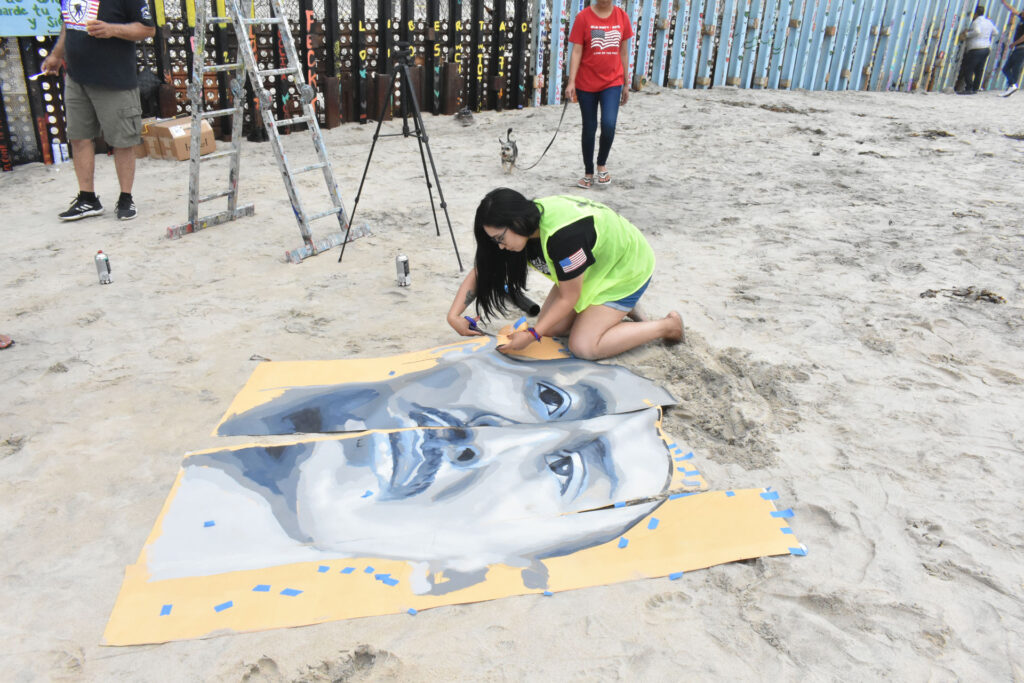 Dr. Lizbeth De La Cruz Santana cuts out a face from the painted canvas laid out on the beach sand in Tijuana.
