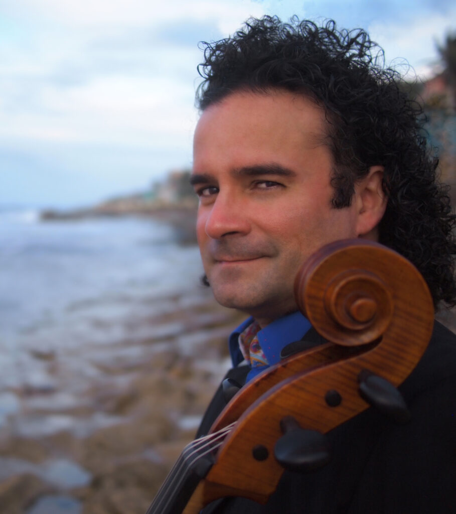 Emilio Colón stands with his cello by the side of a body of water.