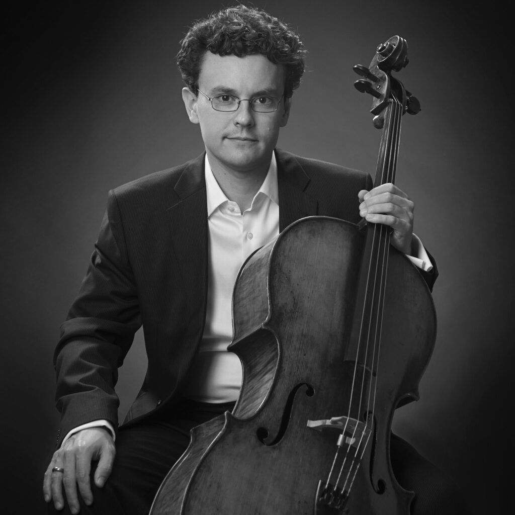 A black and white photo of Jonathan Ruck holding his cello.