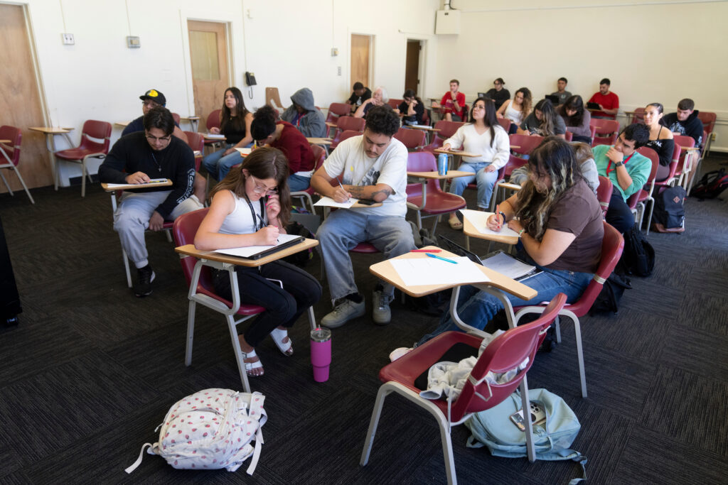 Two debate teams at the front of the class take notes.