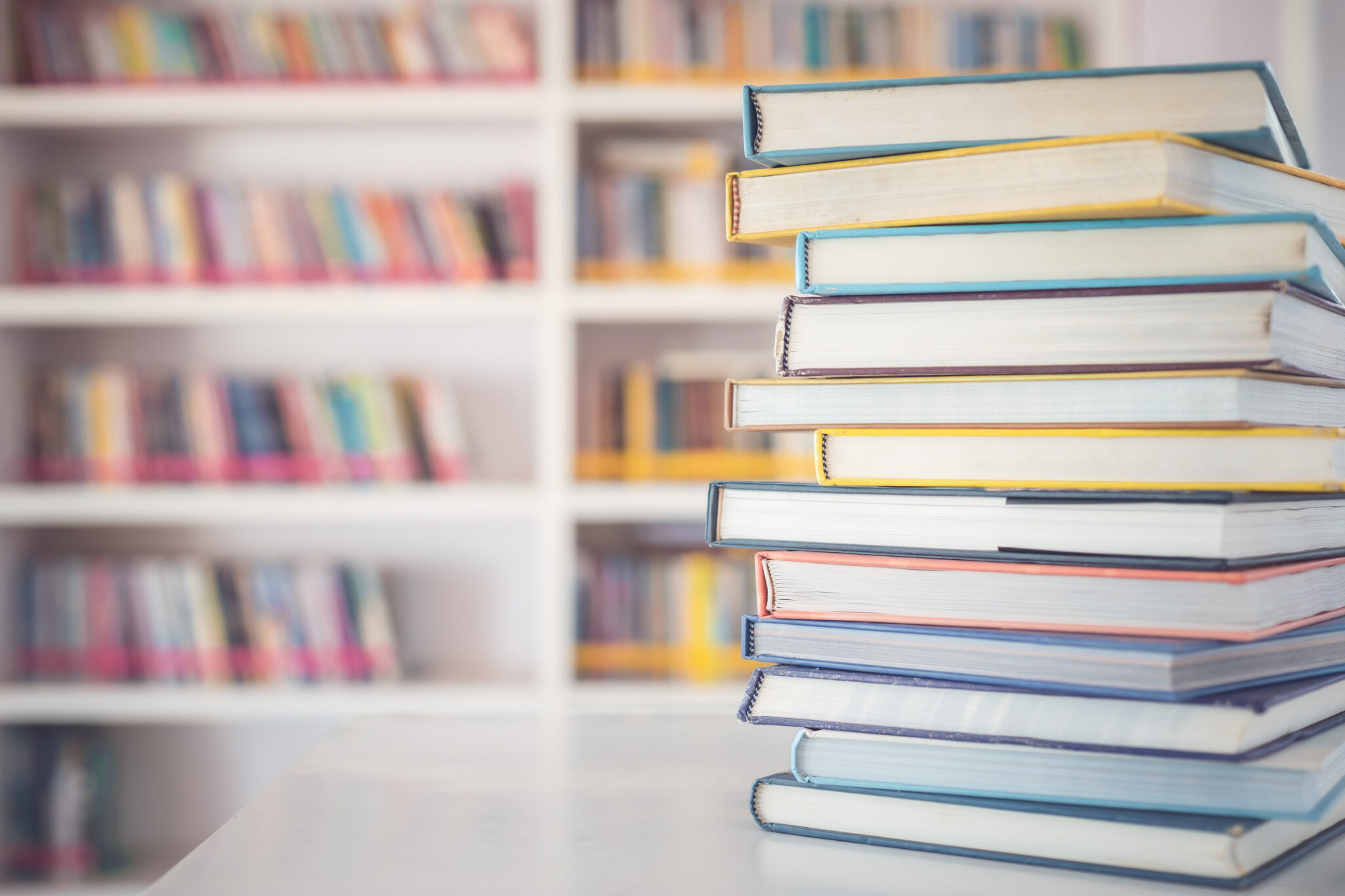 A stack of books on a table with a bookshelf of books behind it.