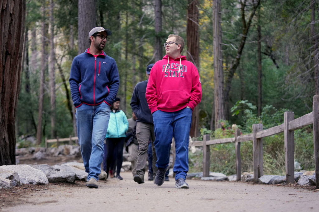 Two people walking and talking on a forest path with others behind them.