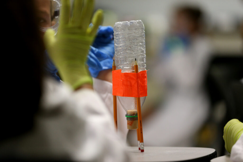 An upside down plastic water bottle with pencils tapped to it for an engineering experiment.