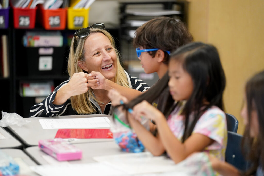 Dr. Corrine Folmer fist pumps a student sitting at a table.