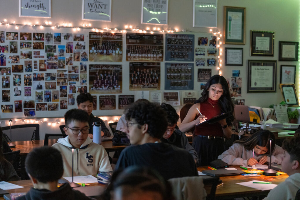 Chrizia Dela Rosa checks her iPad while standing in her classroom surrounded by students.