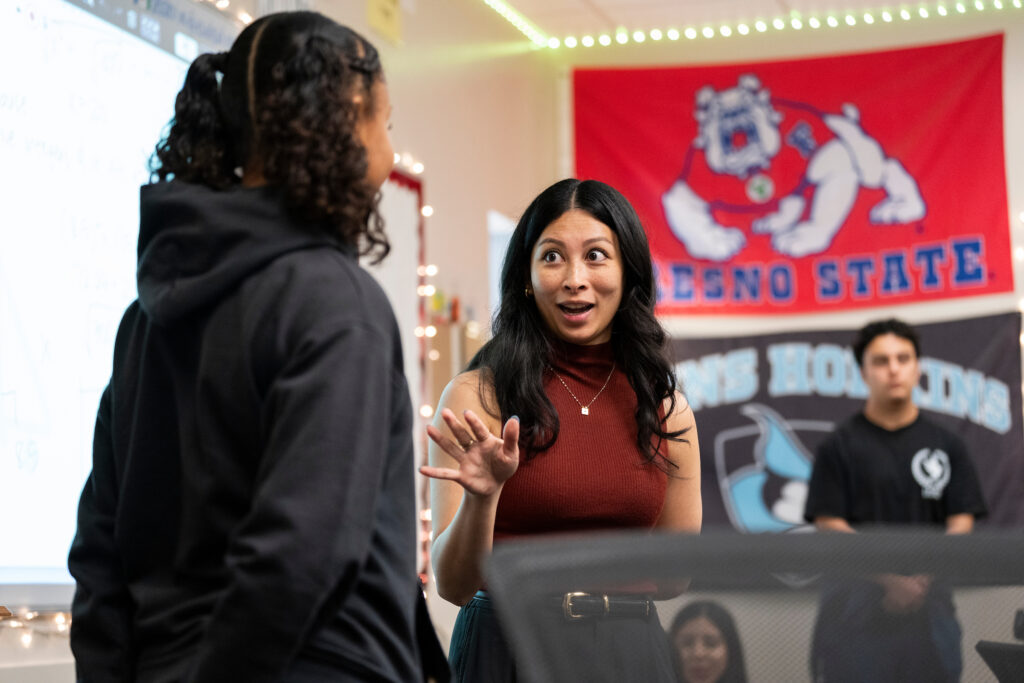 Chrizia Dela Rosa interacts with a student in front of a Fresno State flag in her classroom.